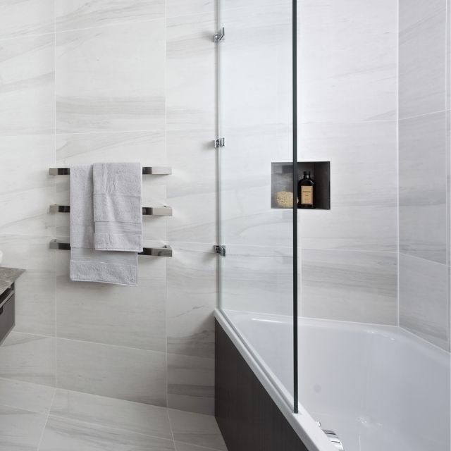 Thermogroup square heated towel rail in polished stainless steel, wall mounted in a bathroom with two towels hanging on it