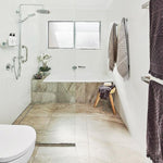 Bathroom with Thermogroup square stainless steel heated towel rail holding hanging towels near bath and shower