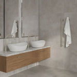 Brushed nickel vertical heated towel rail in a modern bathroom, shown beside a vanity with white towels hanging on the wall