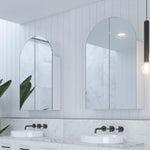 Timberline Church arched shaving cabinet in white, shown recessed above a bathroom vanity with mirrored doors.
