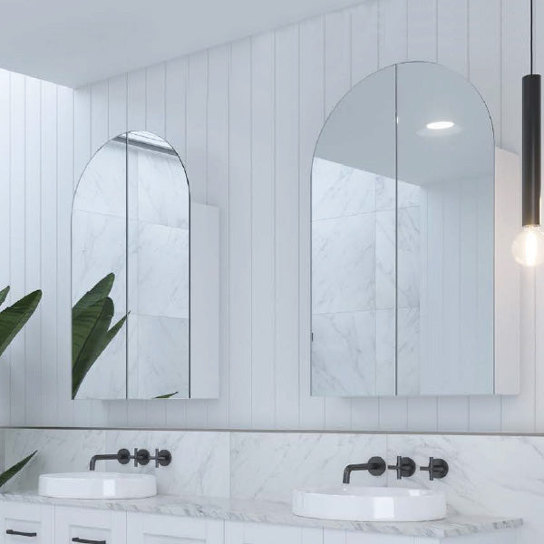 Timberline Church arched shaving cabinet in white, shown recessed above a bathroom vanity with mirrored doors.