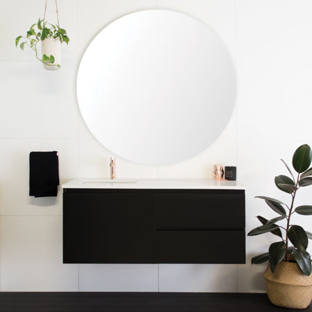 Elegant black vanity cabinet with white countertop against a white wall, accented with a plant beside it