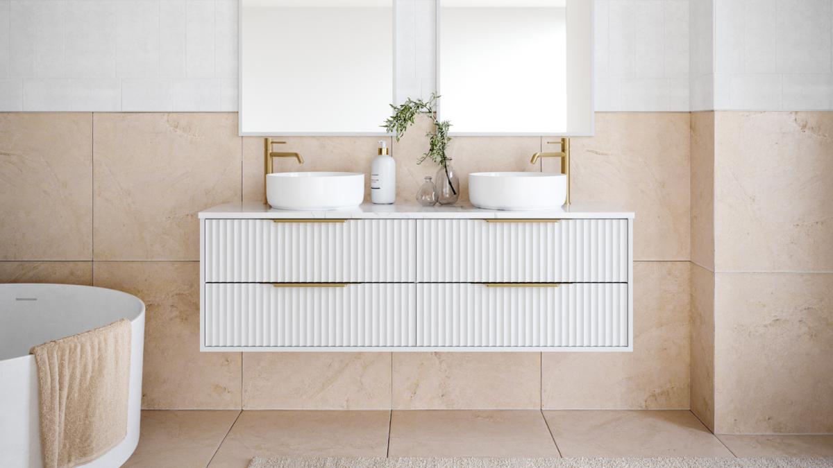 White fluted wall hung vanity with round basins, brushed brass tapware and warm stone tiles