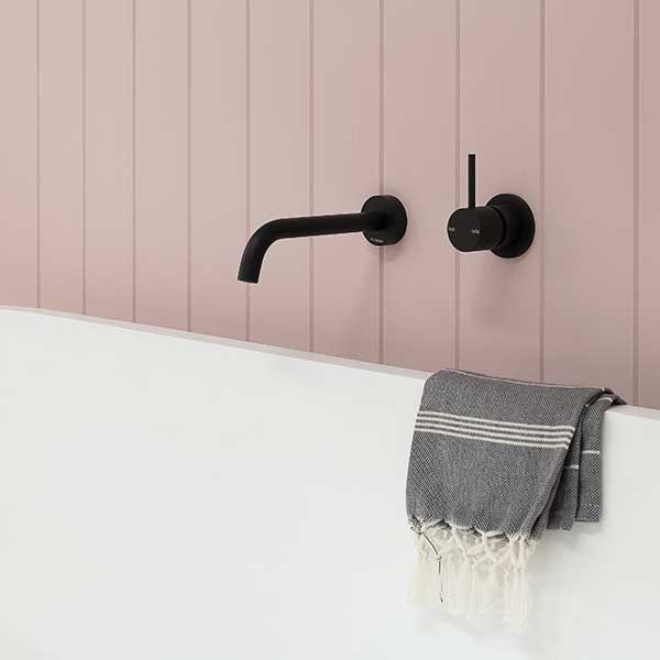 Phoenix Vivid Slimline matte black wall-mounted shower mixer on pink panelled bathroom wall with bath edge and towel