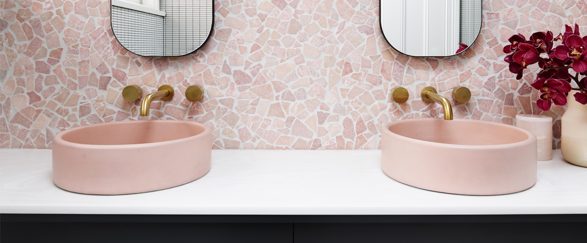 Pink toned bathroom with round peach coloured basins and gold tapware