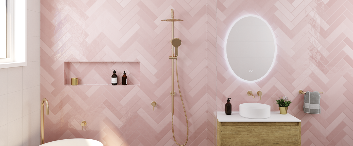 Pink herringbone tile feature wall with round smart mirror, white basin and bath with gold tapware and shower